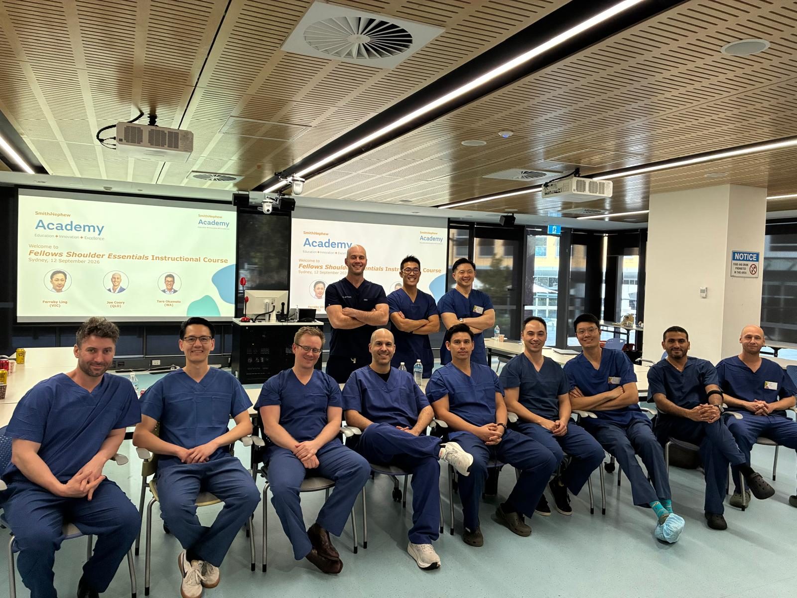 Faculty and fellows at the Fellows Shoulder Essentials Instructional Course, Macquarie University, Sydney, 12 September 2026, in front of the course welcome slide