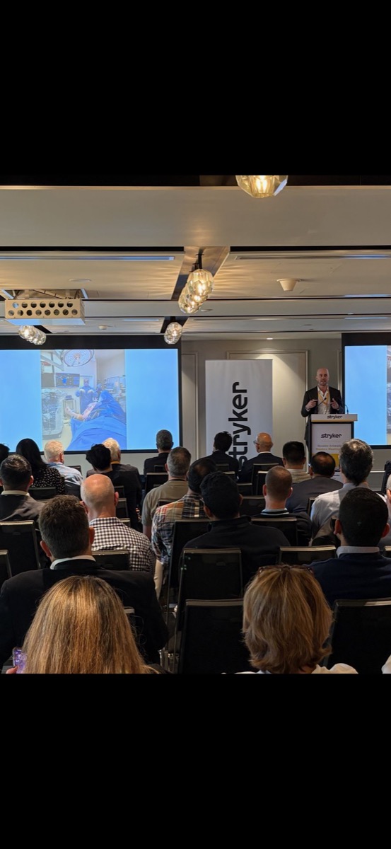 Dr Joe Coory presenting at the Stryker Shoulder Arthroplasty Masters Meeting, Sydney 2026, with an intra-operative image on screen.